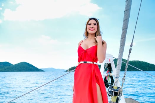 Pretty Asian woman with red dress stand on bow of yacht during boat trip during day time.