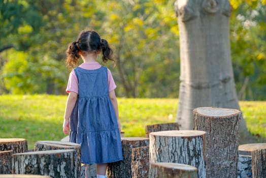 Soft blur of back of little girl walk in park with timber surround her and also morning light shine in front of her.