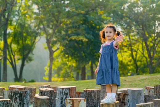 Young asian little girl stand on timber and also wave her hand with morning light in the garden.
