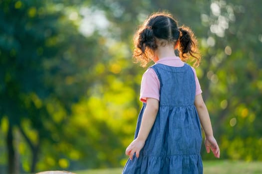 The back of little Asian girl walk in green garden with morning light.