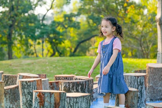 Portrait of little Asian girl smile and walk around the timber in park or garden.