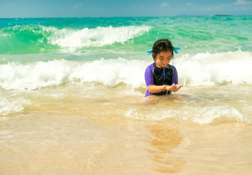 Lovely Asian little girl plays alone on beach with sea wave and she look very happy and fun.