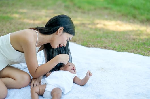 Young Asian beautiful mother play with her little baby on white carpet in the garden with morning light.