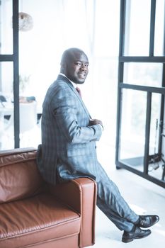 Businessman of 30s in a Gray Checkered Classic Suit Sits on the Back of the Couch in his Living Room. He Turning to Look Back Over His Shoulder at the Camera . Close-up. Copy Space. High quality photo