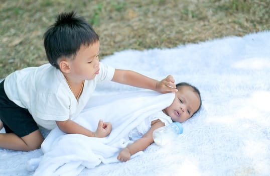 Little boy take care his little sister on white carpet in the garden with day light.