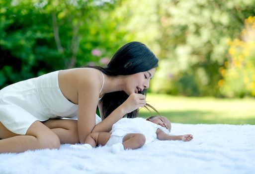 Young Asian beautiful mother play with her little baby on white carpet in the garden with morning light.