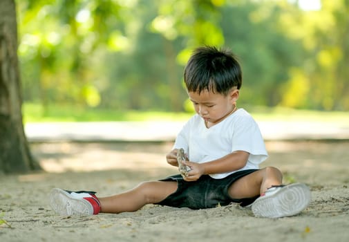 Young little boy sit on the ground and play with himself in the garden with day light.