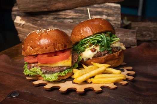 Tasty craft fresh beef burgers with french fries, one with fried walnuts are served on a decorative wooden part of a simple mechanism. Fast food restaurant concept. Street food concept.