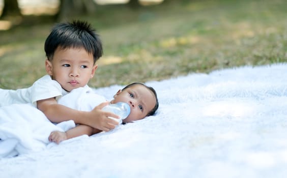 Little boy take care his little sister on white carpet in the garden with day light.