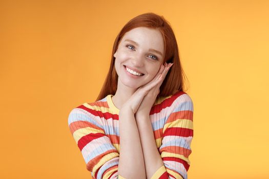 Lovely young flirty redhead european girl smiling broadly excited happy lean palm receive sweet tender present look grateful amused joyfully reacting pleasing moment, standing orange background.