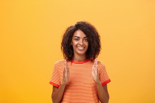 Portrait of charming friendly-looking african american woman with afro hairstyle explaining story with hands and gestures shaping object, holding palms vertical over chest and smiling at camera. Copy space