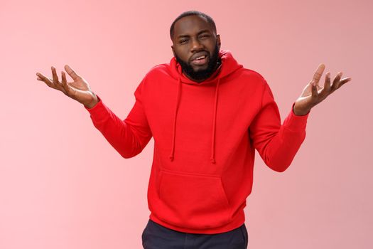 Bothered pissed african american bearded boyfriend in red hoodie arguing standing questioned bothered stupid accusations shrugging raise hands dismay cringing perplexed, pink background.