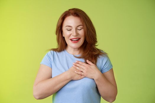 Fascinated cute redhead passionate middle-aged woman sighing lovely touch heart close eyes smiling delighted express admiration temptation feeling appreciation grateful emotions green background.