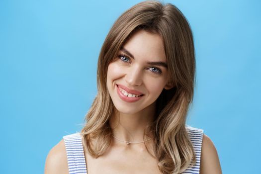 Waist-up shot of charming self-assured authentic woman feeling great accepting own imperfections tilting head smiling broadly at camera and showing cute gapped teeth posing over blue background. Lifestyle.