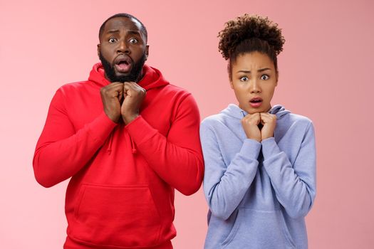 Upset worried two siblings watching together scary disturbing horror movie gasping frowning cringing shock intense emotions press hands chest widen eyes terrified standing nervous pink background.