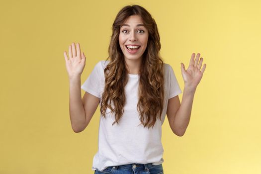 Cheerful glad outgoing cute positive young girl smiling broadly raise both palms waving hands hello greeting gesture welcome friend guest smiling hi gladly invite come inside yellow background. Lifestyle.