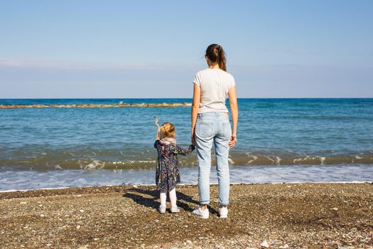 Back view of mother and her little daughter looking at the sea