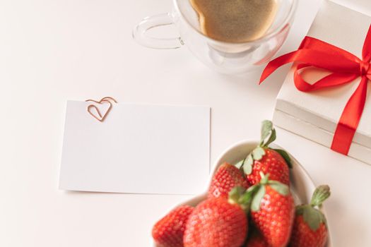 Spring, summer still life composition for valentine day. Blank greeting card mockup scene with heart shaped cup of coffee, strawberries, and roses flowers. Breakfast in bed. Flat lay, top view