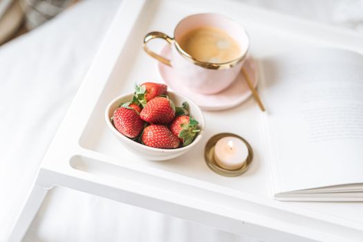 Breakfast in bed. Heart shaped white plate with fresh strawberries, cup of coffee, book and plants flowers. Still life composition. Mother, Valentine day concept.