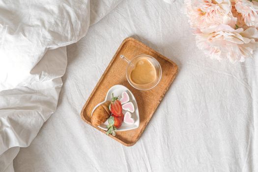 Breakfast for Valentine's Day. Heart shaped white plate with fresh strawberries, cup of coffee, gift and flowers with gift in bed. Still life composition.