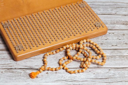 Tibetan Buddhist rosary, called mala or japamala. Brown Sadhu wooden boards with nails for yoga and spiritual practices on the grey background. The concept of meditation, standing on nails, therapy.