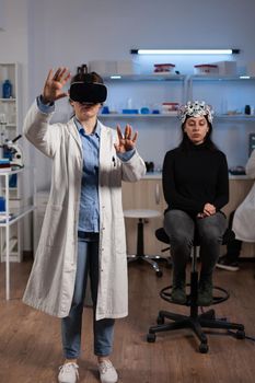 Neurologist doctor with virtual reality headset analyzing brain activity during neuroscience experiment in medical laboratory. Woman patient with eeg scanner having neurology disease