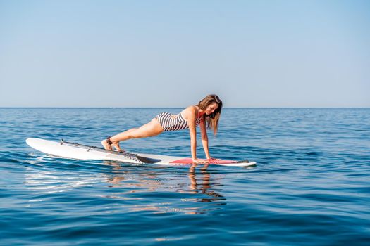 Sporty girl on a glanders surfboard in the sea on a sunny summer day. In a striped swimsuit, it is in the bar. Summer activities by Stortom by the sea.