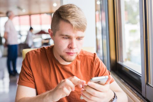 leisure, technology, communication and people concept - close up of man with smartphone texting message in city cafe.