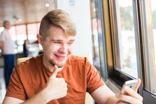 technology, communication and people concept - Young man holding a smart phone with thumbs up.