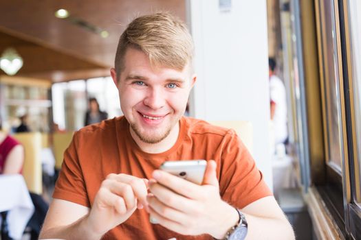 leisure, technology, communication and people concept - close up of man with smartphone texting message in city cafe.