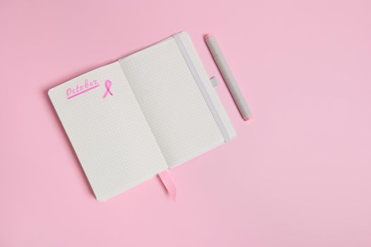 Lettering 1 st October on a diary and a pink ribbon on an empty blank paper sheet, isolated on pink background with copy space. World Breast Cancer Day