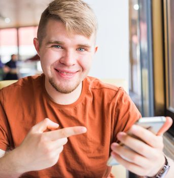 technology, communication and people concept - Young man holding smartphone.