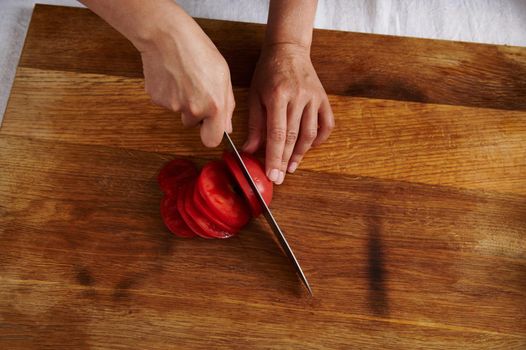 Top view of woman hand cutting tomato on a wooden board