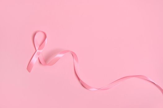 Top view of a long pink satin ribbon, where one end is endless. Breast Cancer Awareness, medical concept isolated on pink background with copy space. October awareness month campaign.