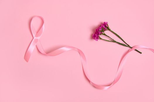 Flat lay of a long pink satin ribbon, where one end is endless and flowers. Breast Cancer Awareness, medical concept isolated on pink background with copy space. October awareness month campaign.