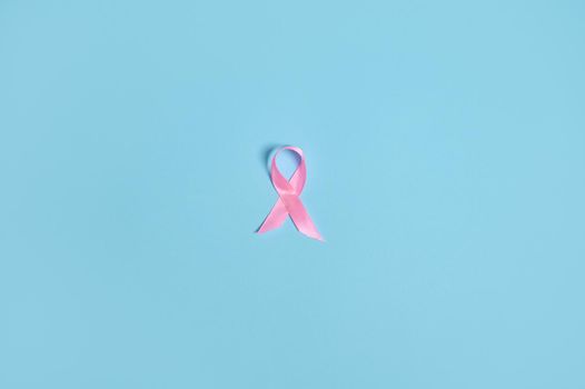 Flat lay of a satin pink ribbon awareness, International symbol of Breast Cancer Awareness Month in October. Isolated over on blue background with copy space .Women's health care and medical concept.