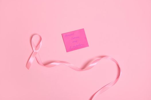 Flat lay of a long pink ribbon with endless one end, and a paper note with lettering 1 October Breast Cancer Awareness Day , isolated on pink background with space for text