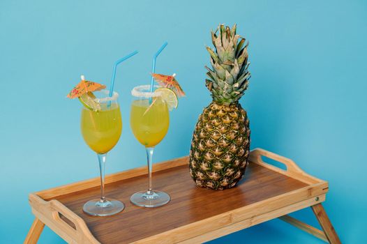 High angle view of pineapple and two glasses with exotic summer cocktails decorated with cocktail umbrella on bamboo serving tray