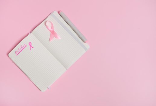 Lettering 1 st October on a diary and a pink ribbon on an empty blank paper sheet, isolated on pink background with copy space. October Pink day, World Cancer Day, national Cancer Survivor Say.