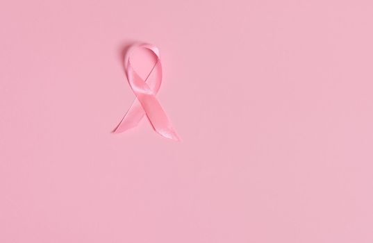 Flat lay of a satin pink ribbon awareness, International symbol of Breast Cancer Awareness Month in October. Isolated over on pink background with copy space . Women's health care and medical concept.