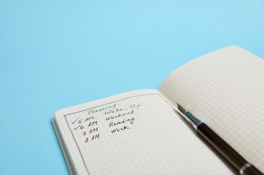 Cropped studio shot of an open organizer with plans for the day, ink pen on blue background with copy space. Time management, business and planning concept