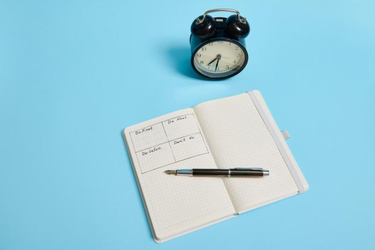 Time management, deadline and concept of proper planning and organization of time: An open organizer notebook with timetable of the day by hour, ink pen, alarm clock on color background, copy space.