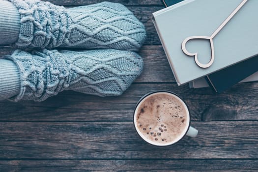 Lonely Valentine's Day. Love at distance, loneliness in self-isolation in the time of coronavirus. Woman resting keeping legs in warm socks with coffee and books. Cozy winter or fall composition