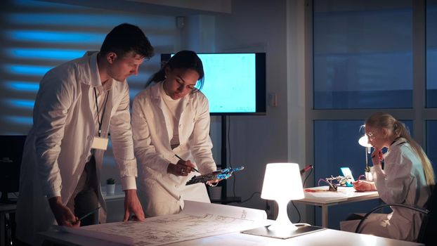 Man and woman in lab coats working in electronics lab with motherboard and control electronics scheme discussing the way of their improvement