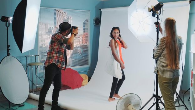 Beautiful african model posing for photo shoot while assistant adjusting the lighting. Photographer taking photos on professional camera.