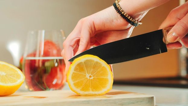 Close up of she cutting off a slice of lemon on wooden kitchen board. Woman preparing something on kitchen.