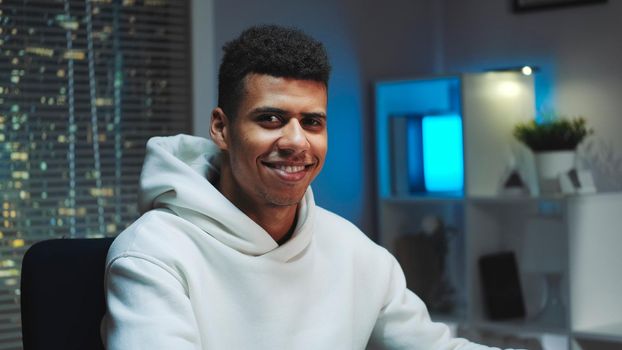 Close-up shot of Handsome black man smiling to the camera while working home on computer. Skyscrapers in the background.