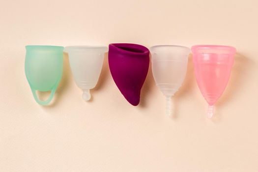 Five menstrual cups of different size, shapes and colors in a row on beige background. Sustainable and comfortable menstruation cycle periods. Reusable eco friendly hygiene products