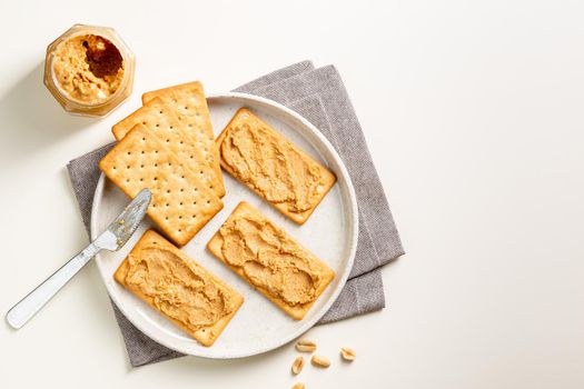 Peanut butter spread on soda crackers on the plate seen from above with knife and jar. Above view