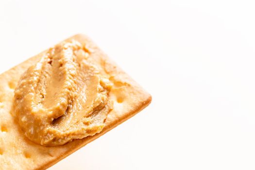 Crunchy peanut butter spread on soda crackers close up on the white background